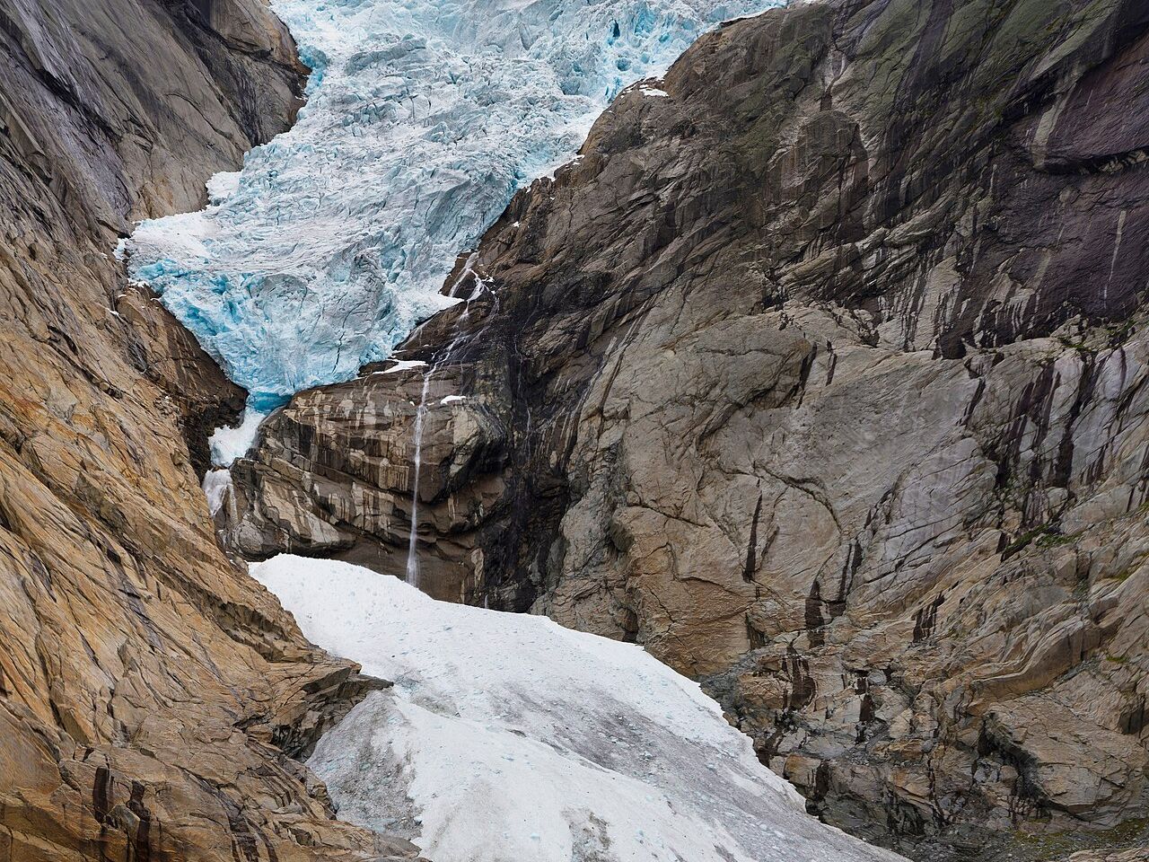 Blue glacier ice of Briksdalsbreen spilling between steep rock walls above old snow