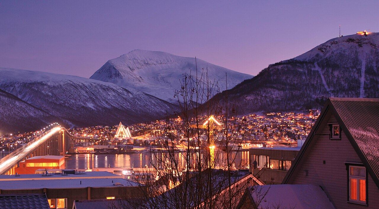 Tromsø on a polar night afternoon under a violet sky, with the lit bridge, the Arctic Cathedral and the town lights below snowy mountains