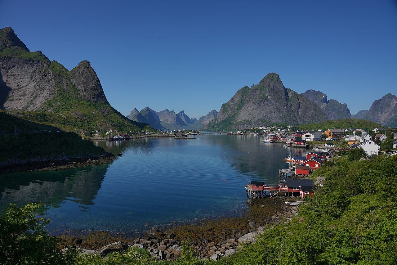 Red fishing cabins on stilts along turquoise water at Reine, under steep granite peaks