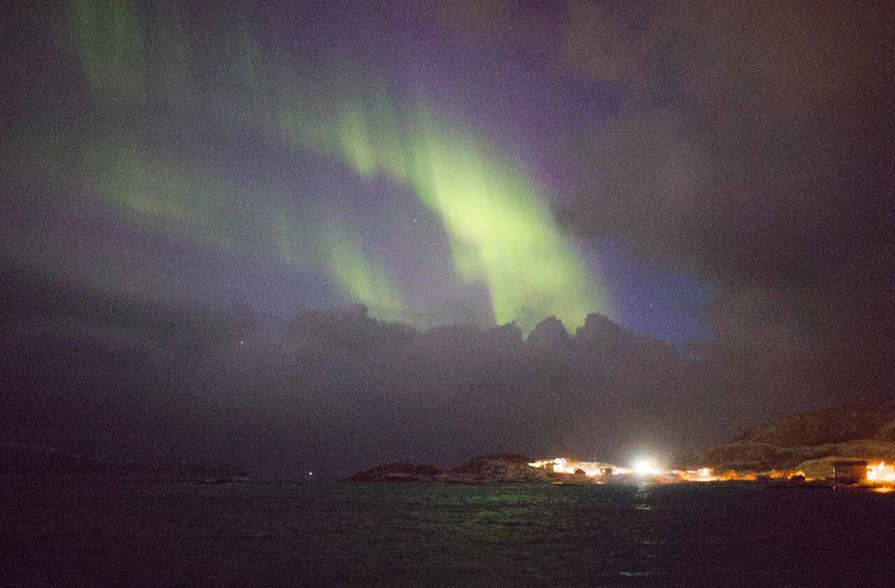 Green and violet northern lights over dark peaks and the sea at Sommarøy